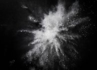 White dust exploding mid air against black background — Stock Photo