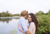 Side view of young couple by lake hugging — Stock Photo