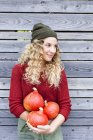 Young woman by wooden shed holding squash, looking away — Stock Photo