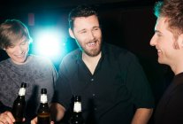 Trois amis masculins buvant de la bière en bouteille dans une boîte de nuit — Photo de stock