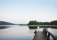 Woman wearing bathrobe with coton de tulear dog looking out from lake pier, Orivesi, Finland — Stock Photo