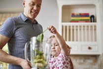 Father and daughter adding ingredients to blender — Stock Photo