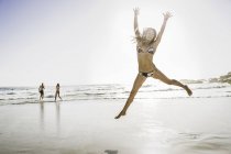 Mid adult woman wearing bikini jumping mid air at beach, Cape Town, South Africa — Stock Photo