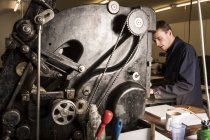 Молодой мужчина, работающий с печатными машинами в типографии — стоковое фото