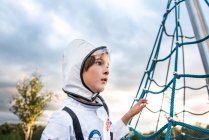 Porträt eines Jungen im Astronautenkostüm, der von einem Spielplatz-Klettergerüst aus blickt — Stockfoto