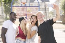 Four adult friends posing for smartphone selfie on basketball court — Stock Photo