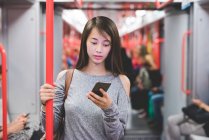 Молодая женщина путешествует в вагоне поезда, читая смс смартфона — стоковое фото