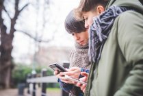 Две сестры смотрят на смартфон, на улице — стоковое фото