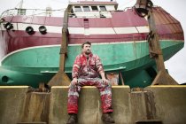 Pintor masculino sentado frente a un barco de pesca en dique seco - foto de stock
