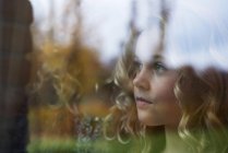 Menina com cabelo loiro longo olhando através da janela — Fotografia de Stock