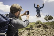 Father photographing teenage son jumping mid air on hiking trip, Cody, Wyoming, USA — Stock Photo