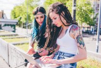 Deux jeunes femmes tapant sur un ordinateur portable dans un parc urbain — Photo de stock
