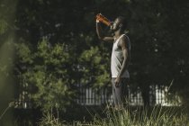Vista laterale uomo in campo bere da bottiglia di plastica — Foto stock
