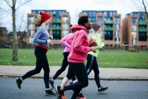 Five female runners running along city sidewalk — Stock Photo