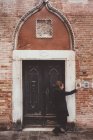 Молодая женщина звонит в дверь старого здания, Венеция, Италия — стоковое фото