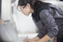 Female technician writing notes in factory — Stock Photo