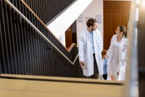 Male and female doctors moving up hospital stairway, talking — Stock Photo