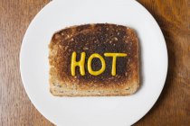 Vue du haut du mot chaud écrit en moutarde sur pain grillé brûlé — Photo de stock