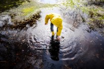 Boy in yellow anorak bending forward in park puddle — Stock Photo