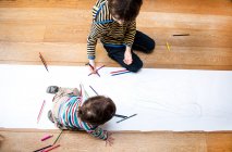Vista aérea del niño y del hermano mayor varones sentados en el dibujo del piso sobre papel largo - foto de stock