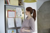 Беременная женщина смотрит календарь на холодильнике — стоковое фото