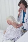 Female doctor listening to senior female patient back with stethoscope — Stock Photo