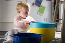 Дитяча дівчинка сидить на підлозі на кухні, граючи з мисками — стокове фото
