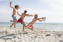 Boy and father chasing brother with rugby ball on beach, Majorca, Spain — Stock Photo
