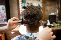 Rear view of young man in barbershop having haircut — Stock Photo