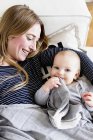 Baby girl reclining on sofa with mother sucking comfort blanket — Stock Photo