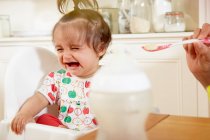 Bébé fille pleurer tout en étant nourri petit déjeuner par mère — Photo de stock