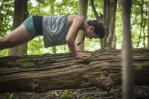 Woman doing push ups on log in forest — Stock Photo