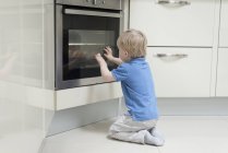 Young boy sitting in front of oven, looking through glass, rear view — Stock Photo