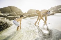 Отец и сын играют в луже воды рядом со скалами — стоковое фото