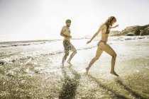 Mid adult couple wearing bikini and swimming shorts splashing in sea, Cape Town, South Africa — Stock Photo