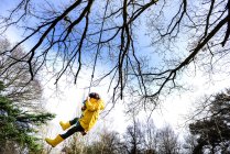 Junge im gelben Anorak schwingt von Parkbaum — Stockfoto