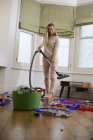 Mid adult woman with vacuum cleaner and scattered toys in living room — Stock Photo