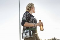 Жінка середнього віку, що носить пляшку пива та старовинну камеру в парку — стокове фото