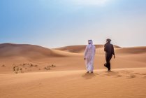 Couple wearing traditional middle eastern clothes walking in desert, Dubai, United Arab Emirates — Stock Photo