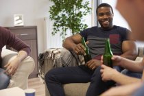 Группа мужчин, сидящих в гостиной и держащих бутылки пива с улыбкой — стоковое фото