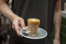 Colpo ritagliato di barista che tiene il bicchiere di caffè in caffè — Foto stock