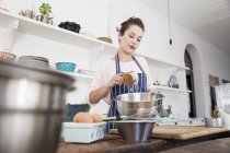 Jeune femme versant de la farine dans un bol au comptoir de cuisine — Photo de stock