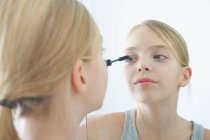 Over the shoulder mirror image of girl applying mascara — Stock Photo