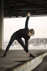 Female runner bending forward stretching on warehouse platform — Stock Photo