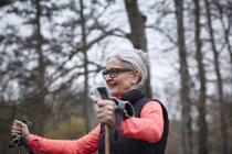 Зрелая женщина тренируется в парке, стоит с северными полюсами — стоковое фото
