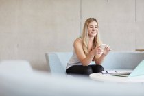 Young female student sitting on study space sofa reading smartphone texts at higher education college — Stock Photo