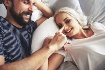 Paar liegt im Bett, albert herum, Mann stochert weibliche Nase — Stockfoto