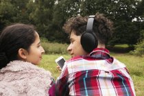 Brother and sister, sitting outdoors, listening to music, rear view — Stock Photo