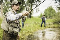 Man fly fishing with family in river — Stock Photo