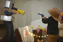 Hombre mayor en traje de robot disparando armas de juguete con nietos vestidos - foto de stock